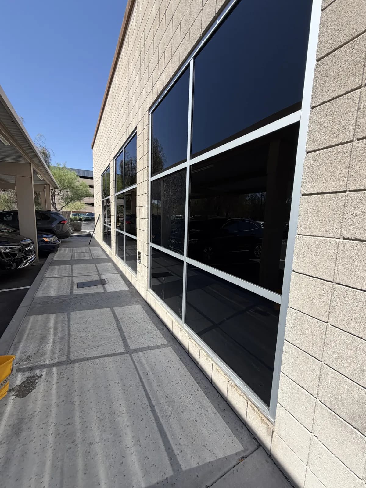 Tan block commercial building with large dark-tinted window panels along a covered parking walkway, the glass clean and reflective under a blue sky