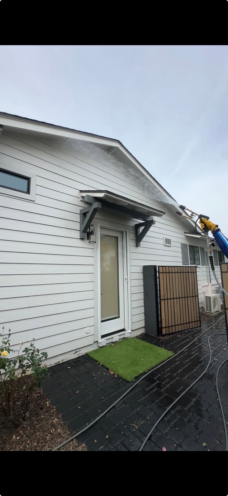 Soft-washing a Phoenix home exterior, water sheeting off the eaves